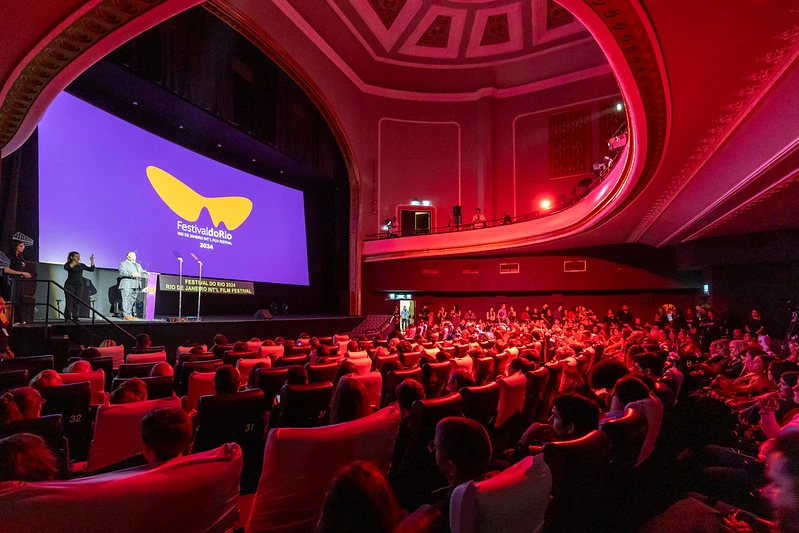 A imagem mostra um teatro com lotação máxima e um telão escrito "Festival do Rio".