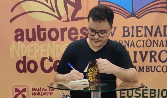 A imagem mostra Moacir Fio autografando um exemplar do seu novo livro.